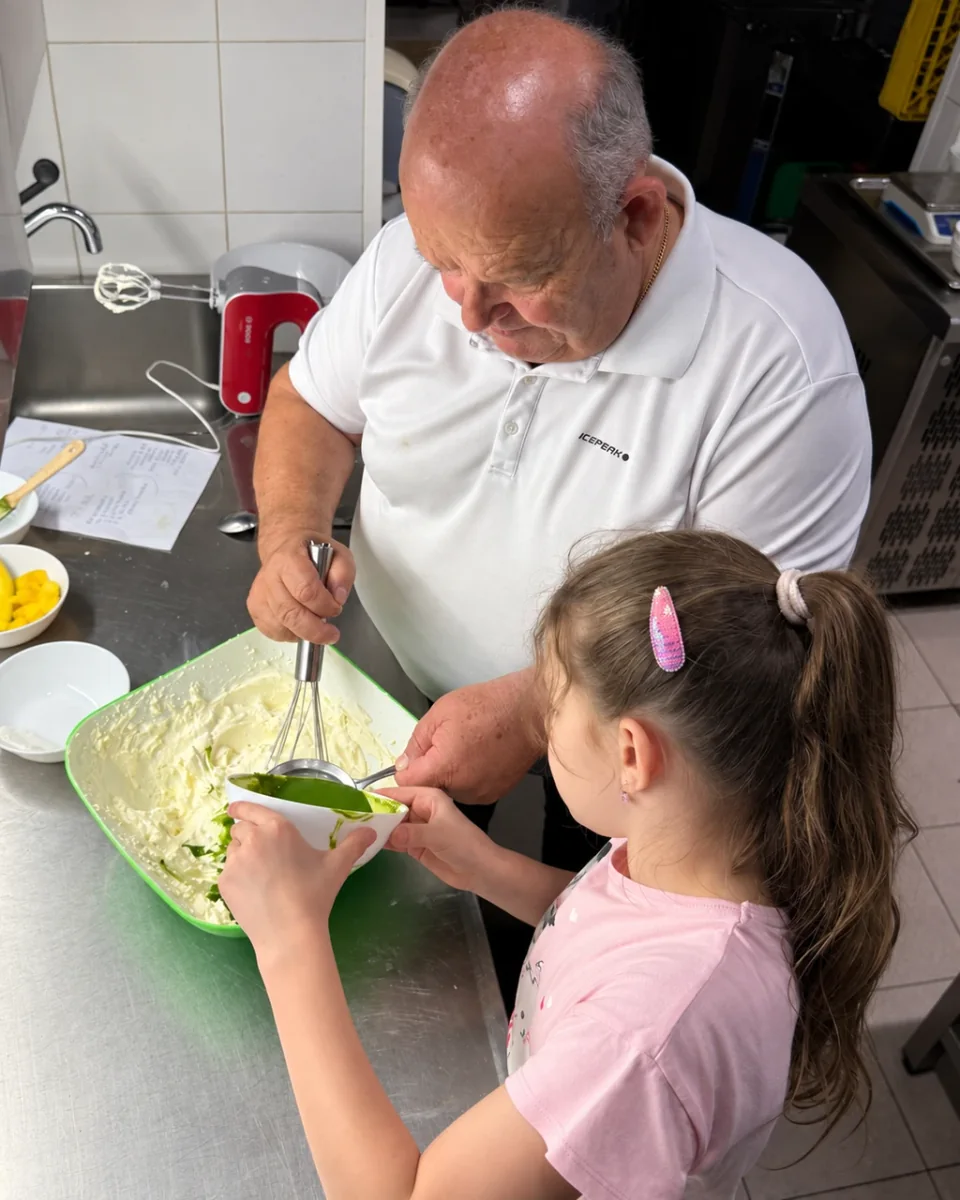 An older man and a young girl preparing cream together in a catering kitchen